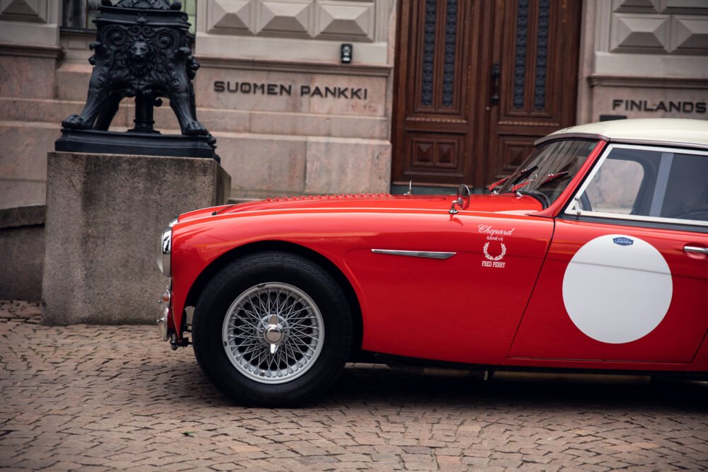 Red vintage car parked outside Suomen Pankki building.