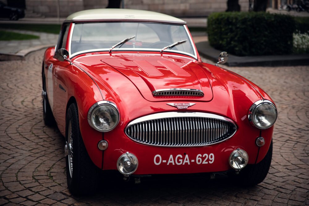 Red vintage Austin-Healey sports car on cobblestone street.