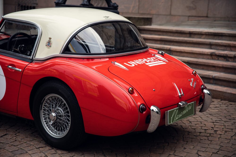 Vintage red and white Maserati parked on cobblestone street.