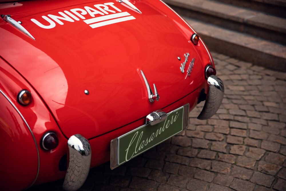 Red vintage car with "Unipart" logo and "Classicari" license plate.