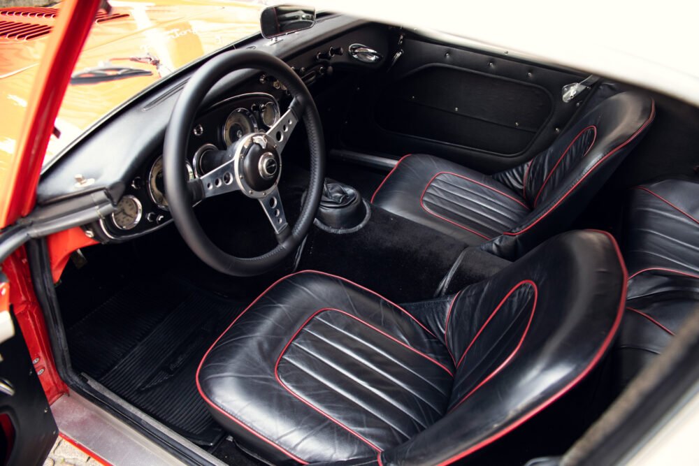 Classic car interior with red accents and steering wheel.