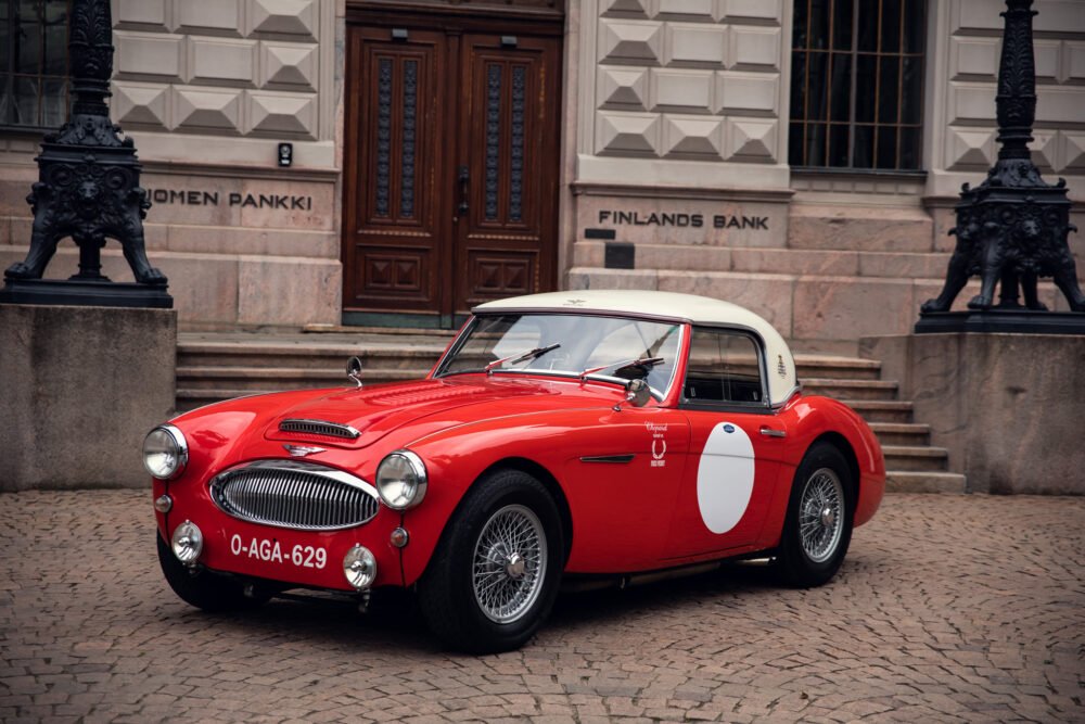 Red vintage car parked outside Finland's Bank building.