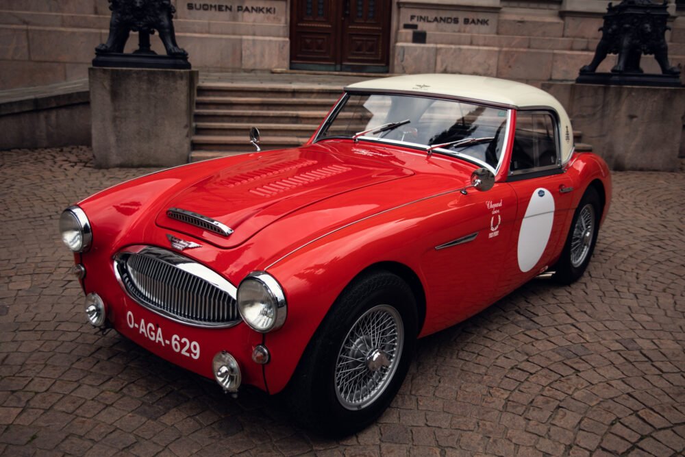 Vintage red Austin-Healey sports car by bank building.