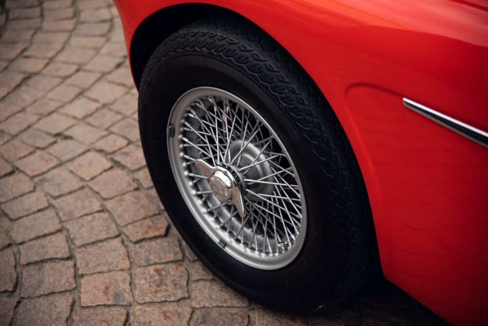 Red classic car wheel on cobblestone.