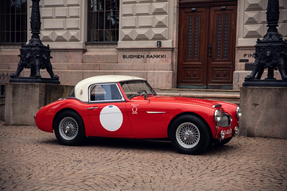 Vintage red sports car parked outside historic building.