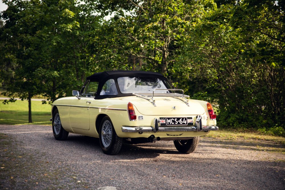 Vintage yellow convertible car parked in wooded area.