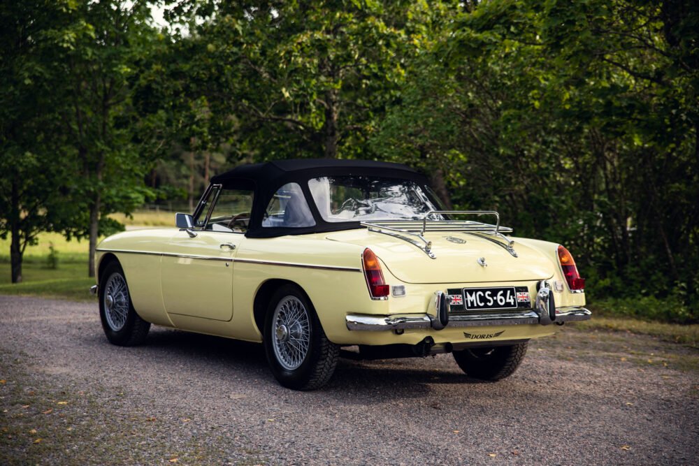 Vintage yellow convertible car parked in green landscape.