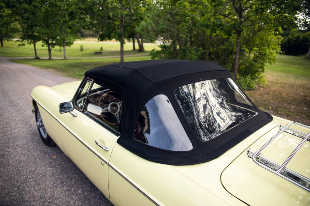 Vintage yellow convertible car on tree-lined road.