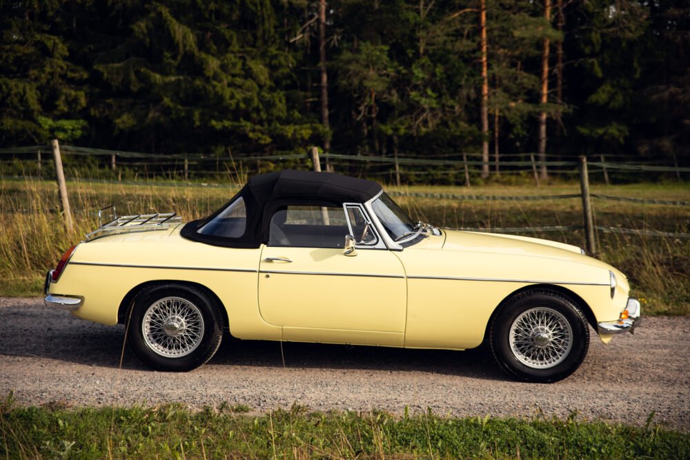 Vintage yellow convertible car parked outdoors near forest.