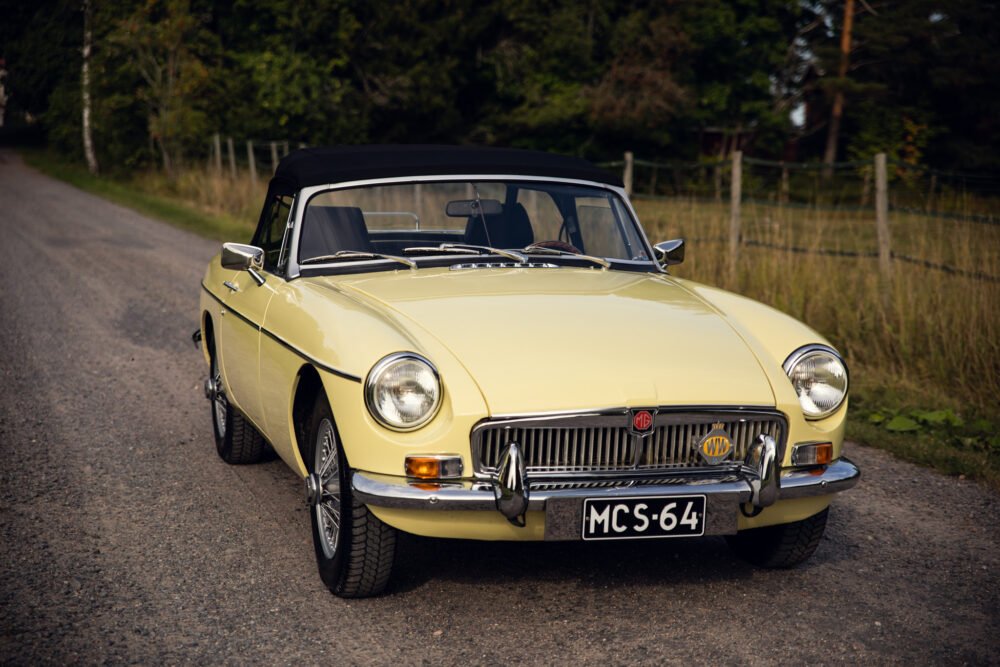 Vintage yellow MG convertible on rural road.