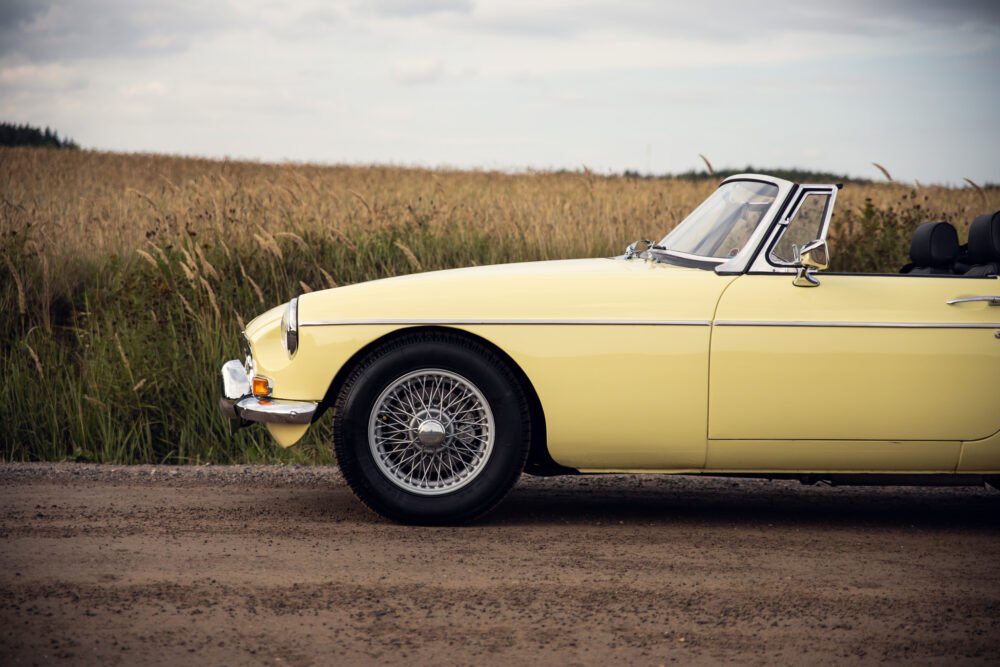 Yellow classic car beside golden wheat field.