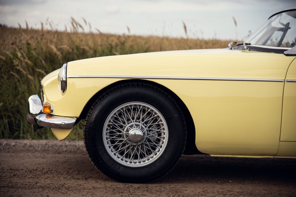 Yellow vintage car with wire wheels on rural road.