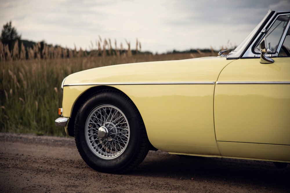 Yellow vintage car with wire wheels on rural road.