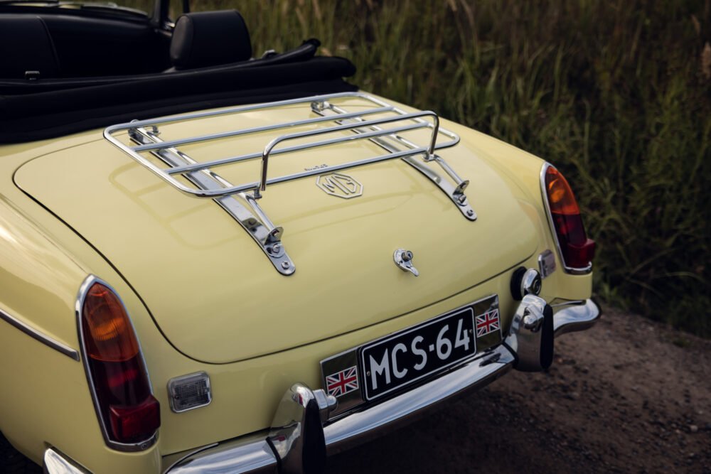 Vintage yellow MG car with rear luggage rack.