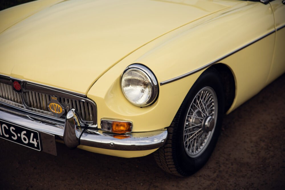 Yellow vintage MG car front detail on road.