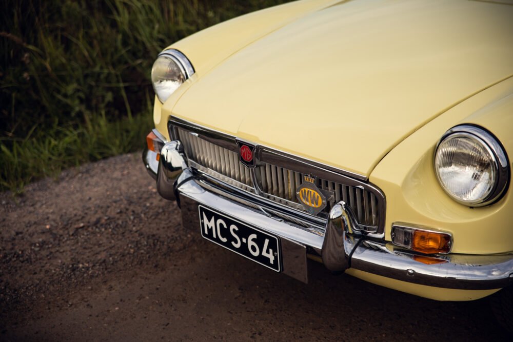 Yellow vintage MG car front detail on road.