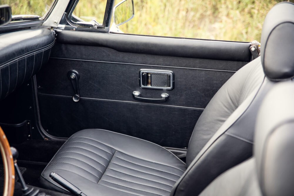 Vintage car interior with leather seats and chrome handles.