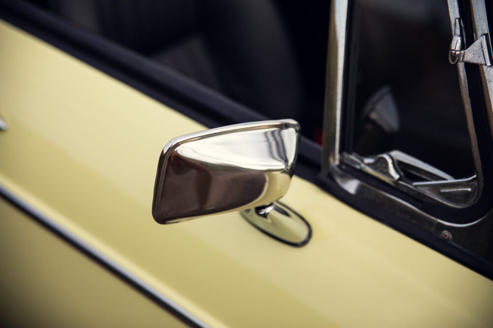 Vintage car chrome side mirror on yellow door.