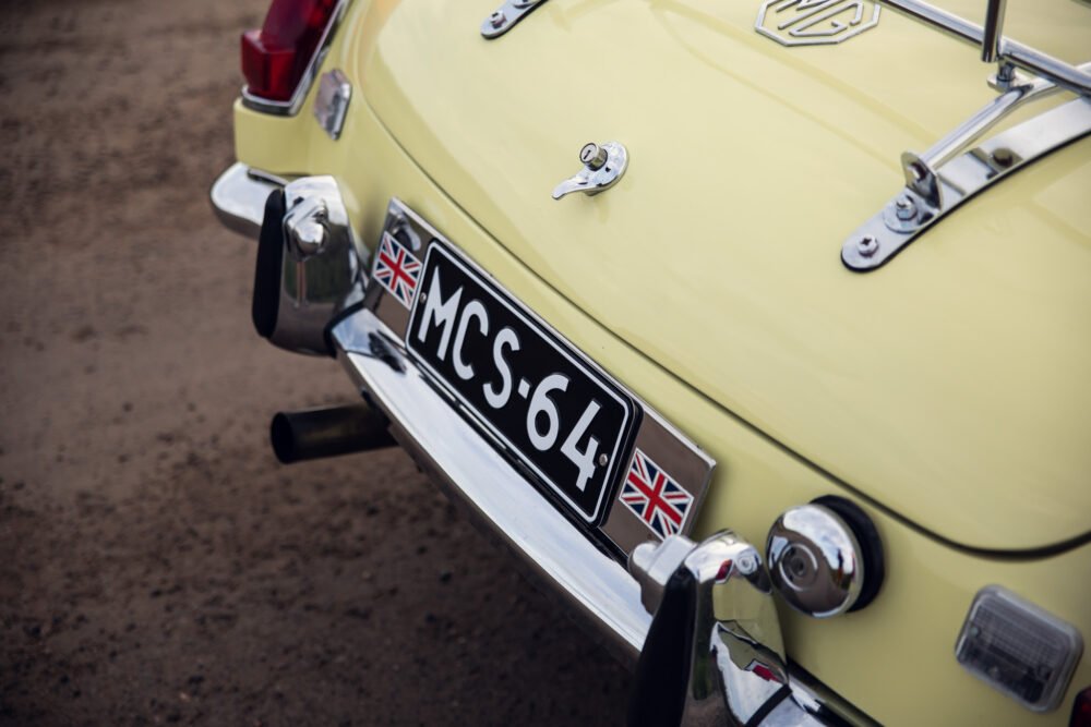 Yellow vintage car with British flag on license plate.