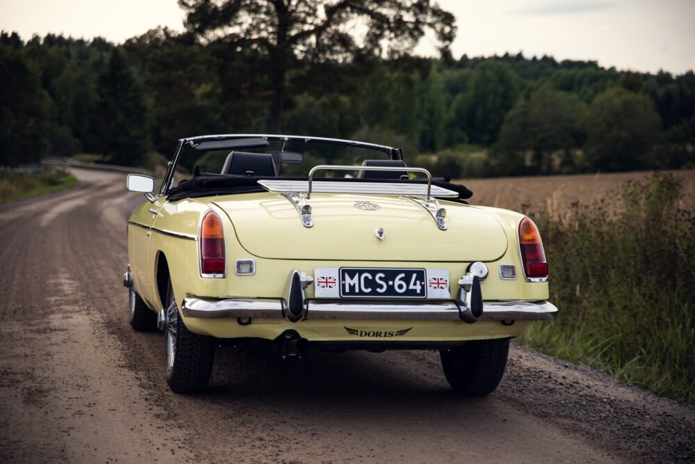 Yellow MG convertible on rural road, rear view.