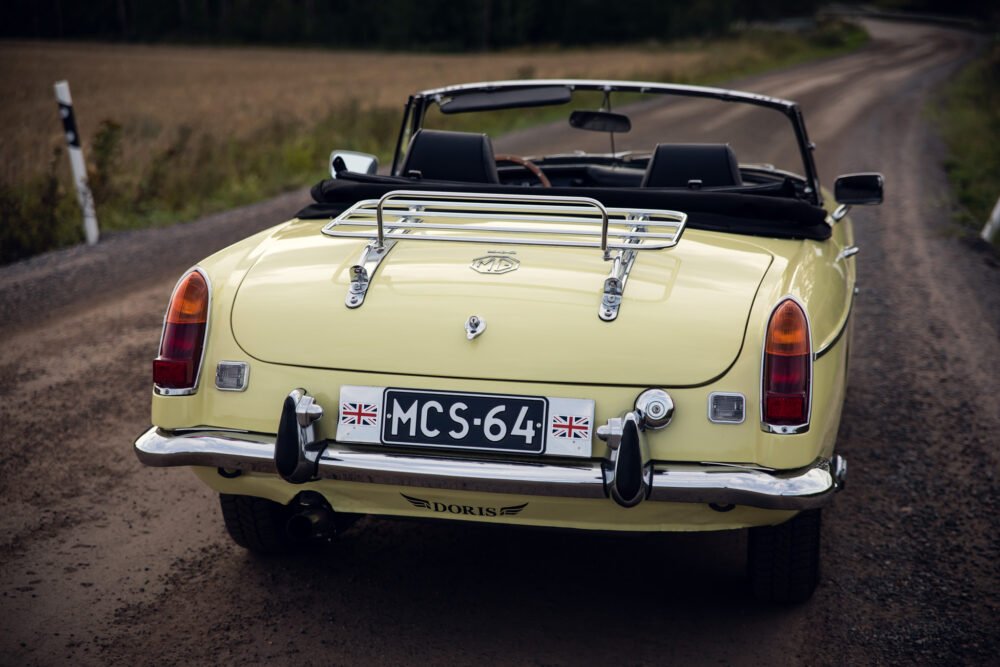 Vintage yellow MG convertible on rural road.