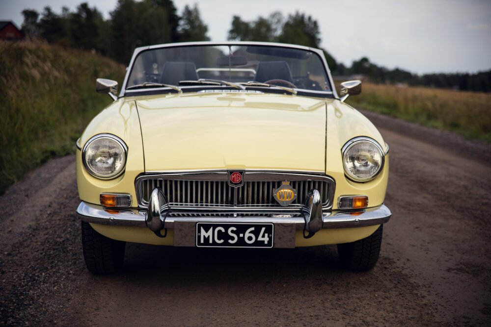 Vintage yellow MG convertible on rural road.