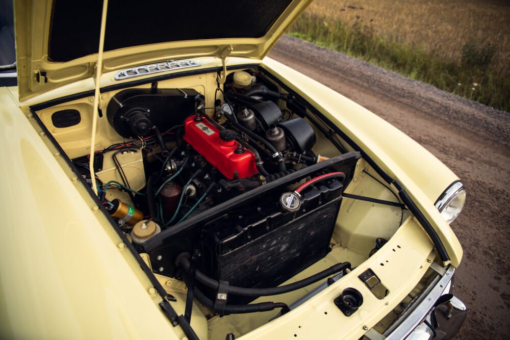 Vintage yellow car engine compartment open on dirt road.