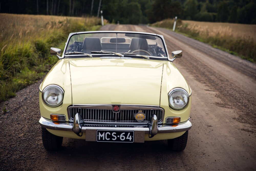 Yellow vintage MG convertible on rural road.