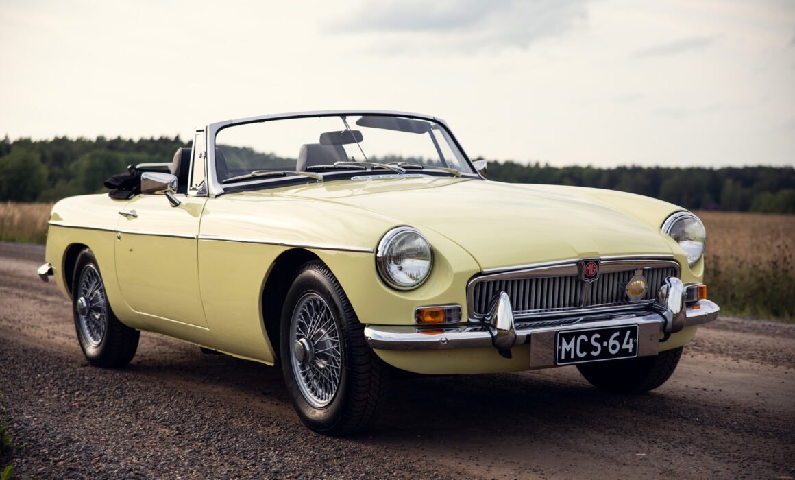 Vintage yellow MG convertible car on countryside road.