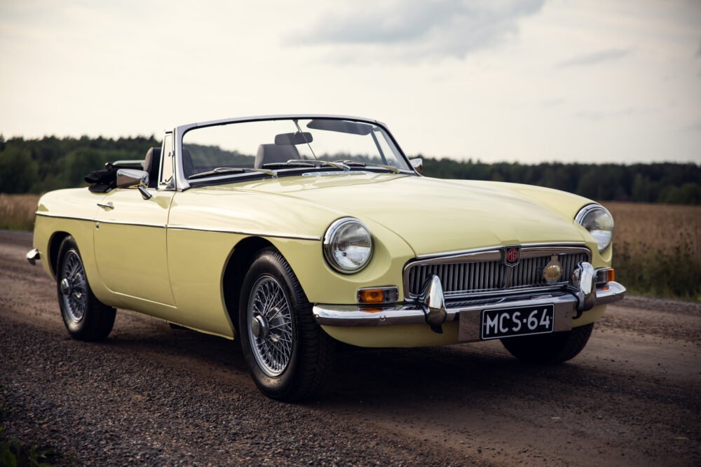 Vintage yellow MG convertible on rural road.