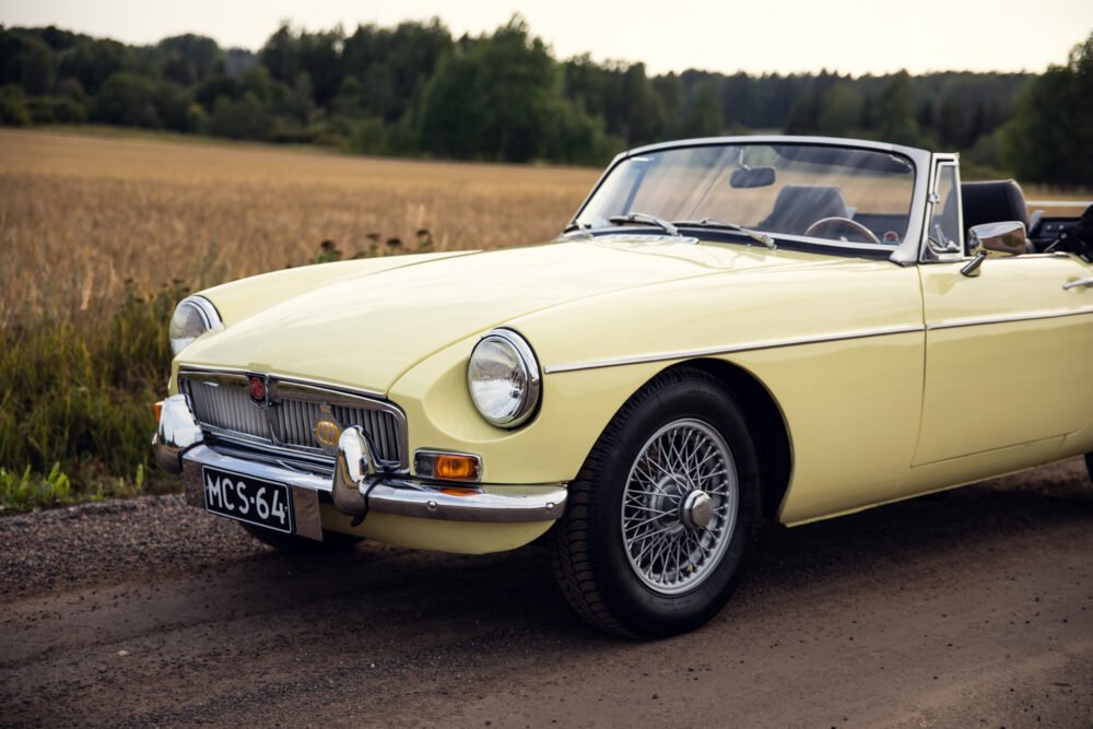 Vintage yellow MG convertible parked by countryside field.