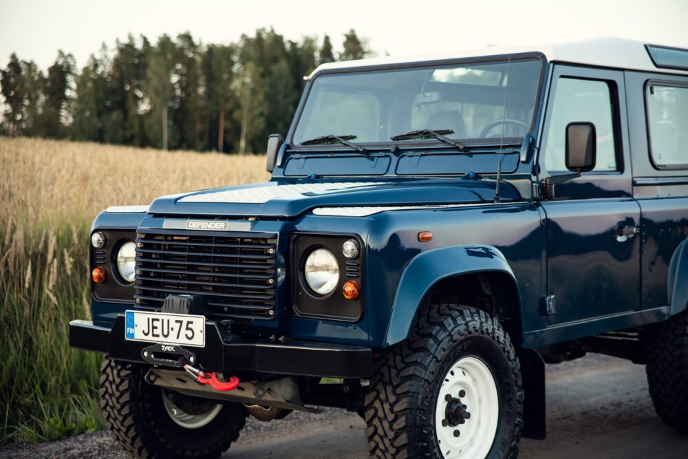 Blue Land Rover Defender parked in rural setting.