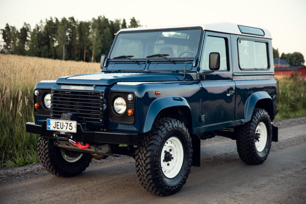 Blue Land Rover Defender in countryside setting.