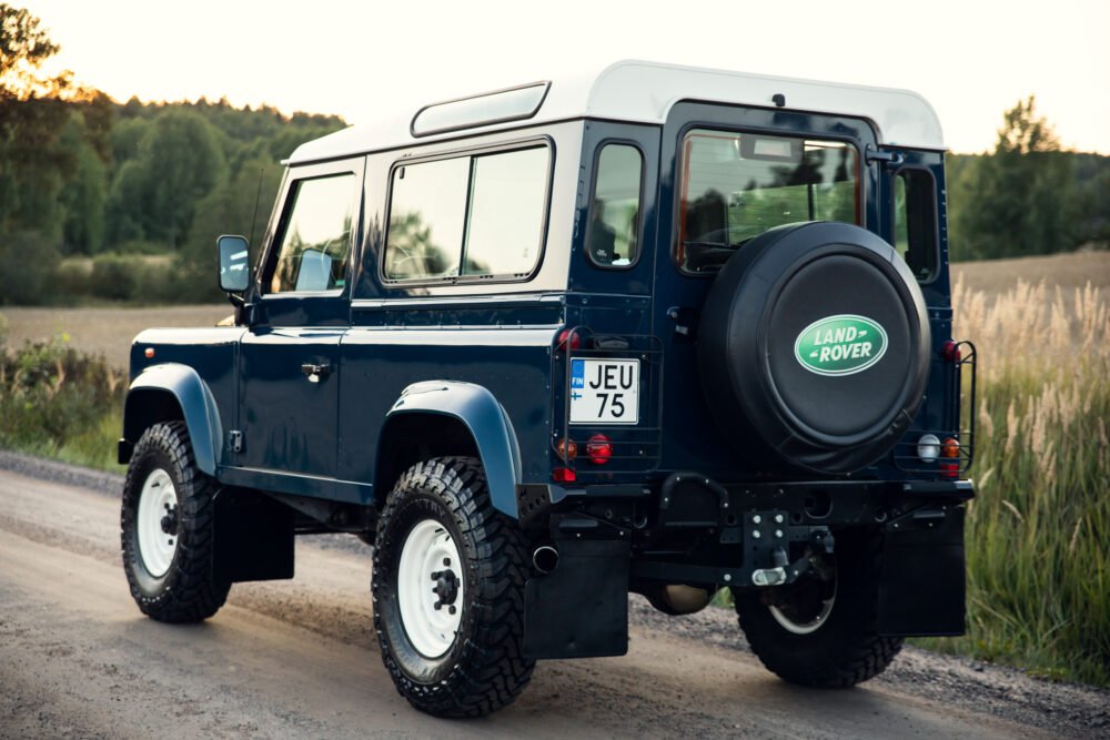 Blue Land Rover Defender on rural road at sunset.