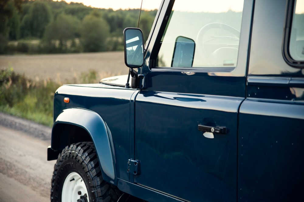 Blue off-road vehicle parked near rural road at sunset.