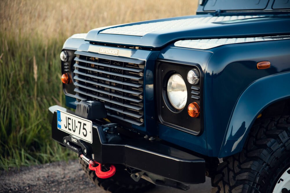 Blue Land Rover Defender in grassy field.