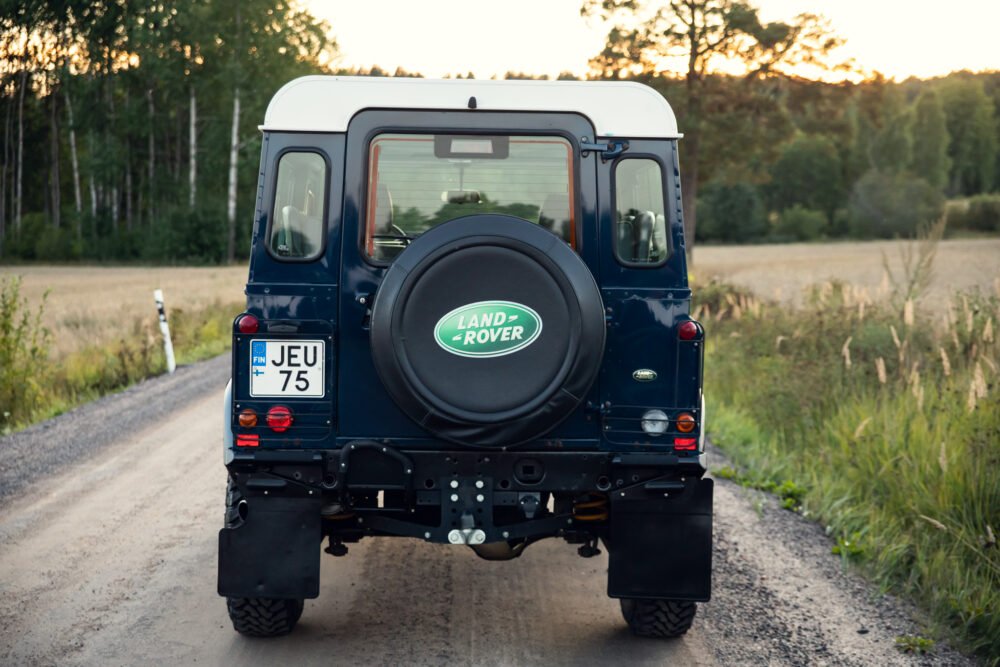 Land Rover Defender on scenic forest road at dusk.