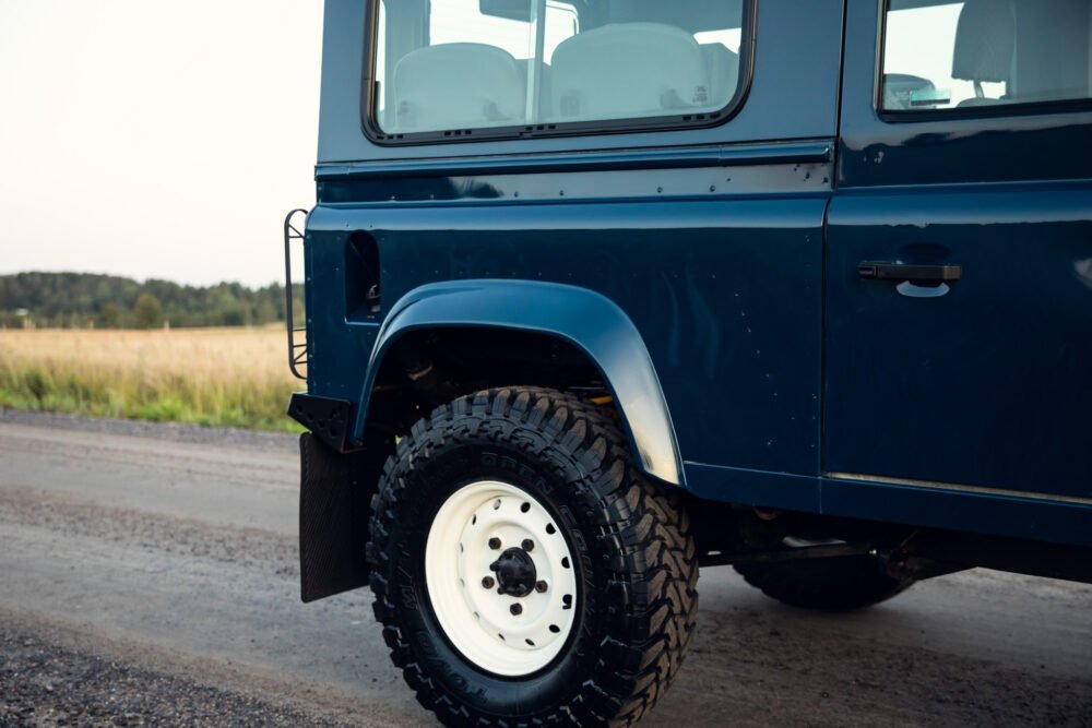 Blue SUV with off-road tires parked by field.