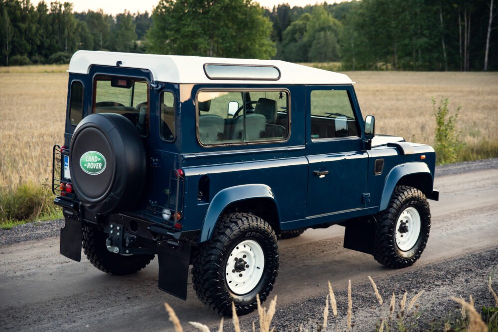 Blue Land Rover Defender parked on country road.