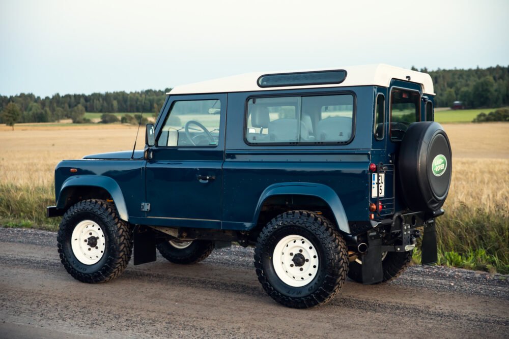 Blue Land Rover Defender parked in rural setting.