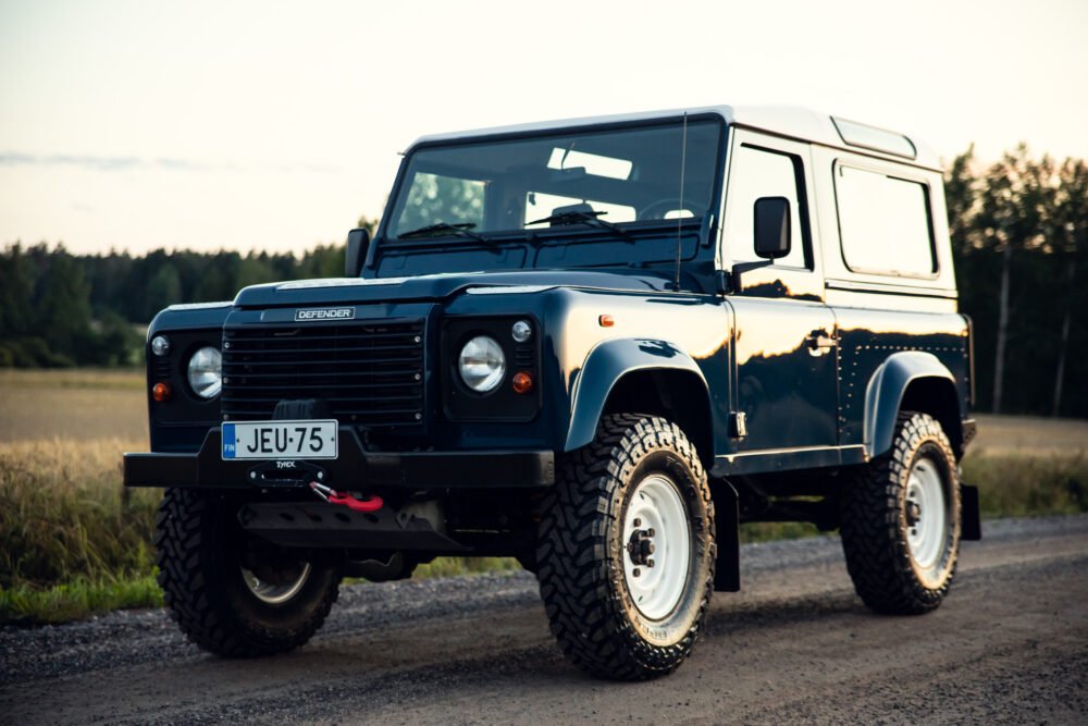 Blue Land Rover Defender on rural road at dusk.