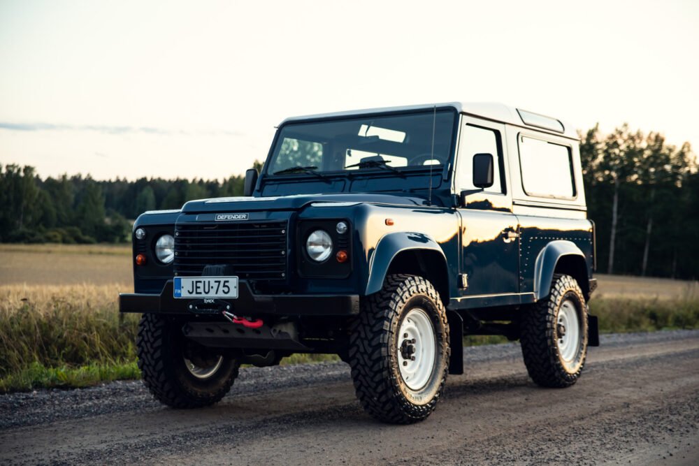 Blue Land Rover Defender on rural road at dusk.