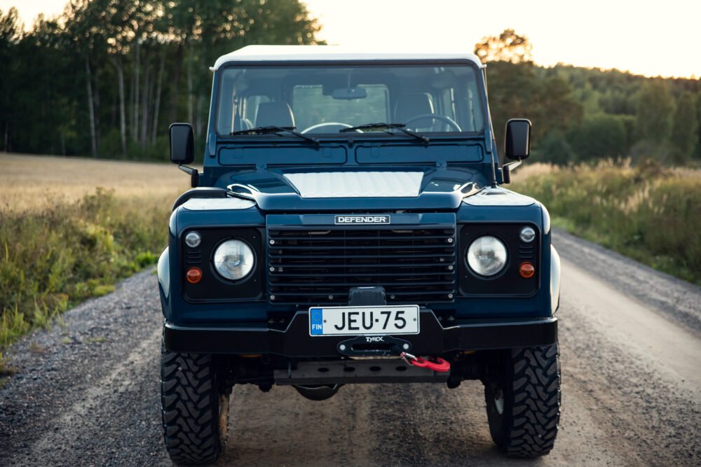 Blue Land Rover Defender on rural road at sunset.