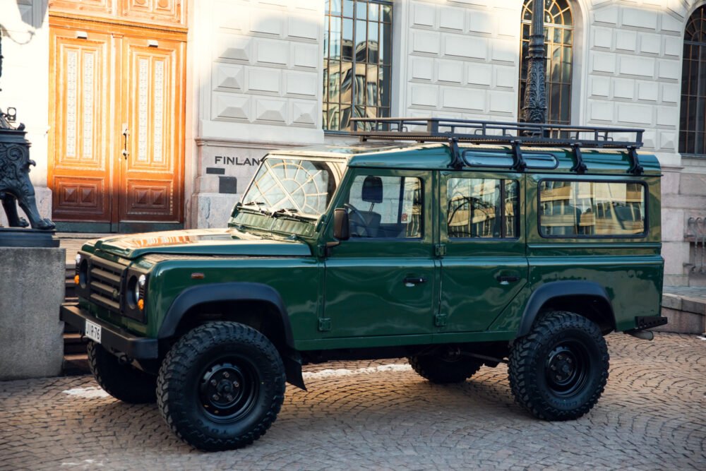 Green SUV parked on cobblestone street near building.