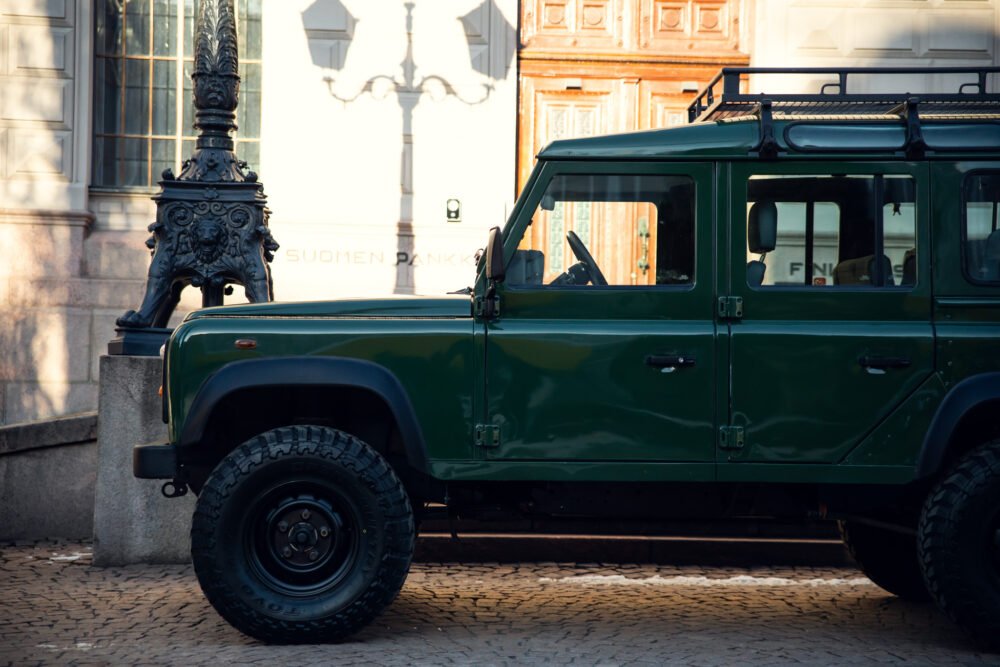 Green SUV parked near ornate lamp post and building.