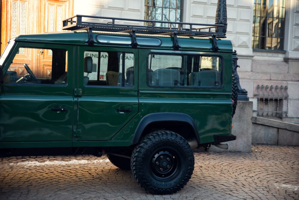 Green off-road SUV parked on cobblestone street.