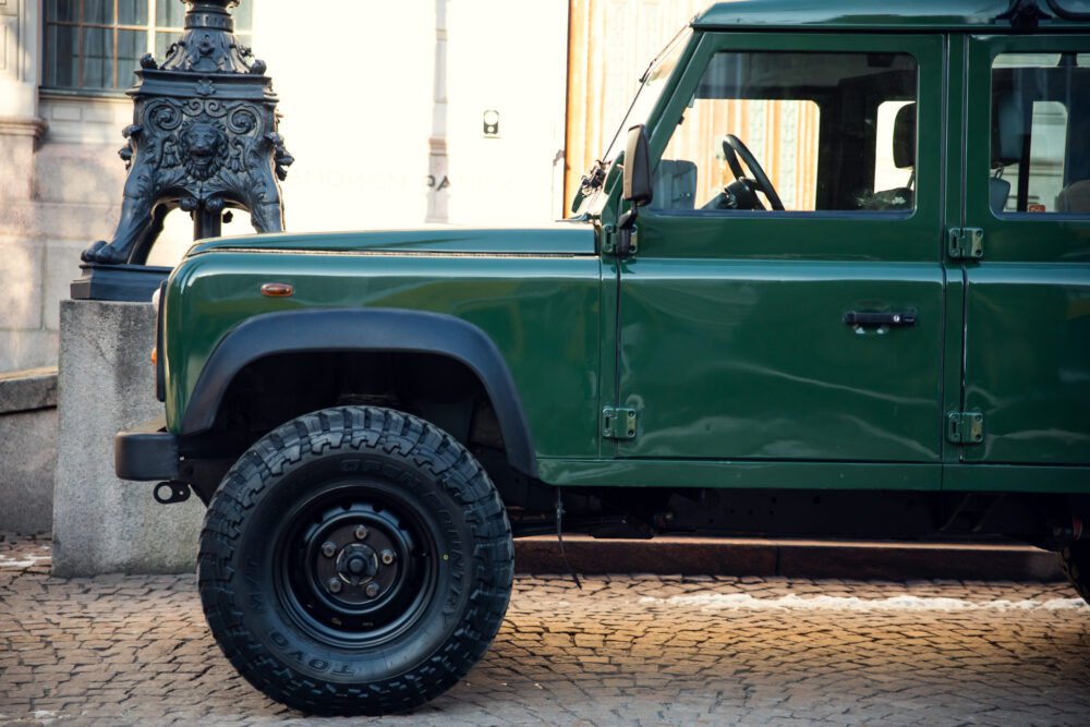 Green off-road vehicle parked near ornate street lamp.