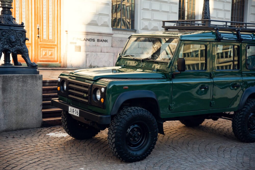 Green off-road vehicle parked near elegant building.