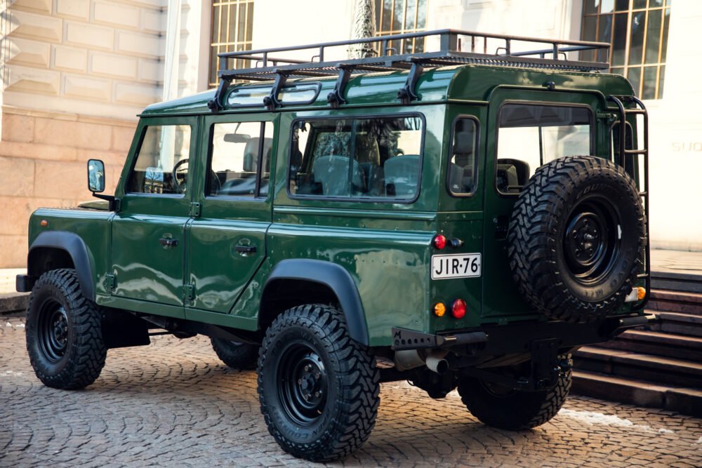 Green Land Rover Defender parked on cobblestone street.