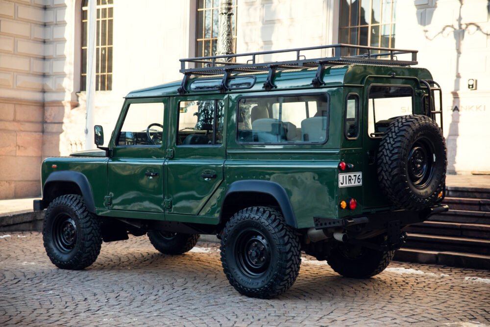 Green Land Rover Defender parked near historical building.